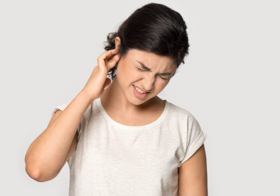 Unhealthy indian millennial lady suffering from strong earache, head shot portrait. Stressed frowning young ethnic girl plugging ear, feeling painful discomfort isolated on grey studio background.